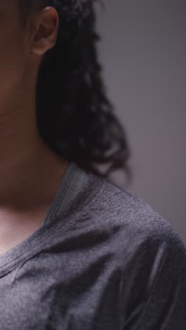 Vertical-Video-Close-Up-Studio-Shot-Of-Woman-Wearing-Sports-Clothing-Against-Dark-Background-Warming-Up